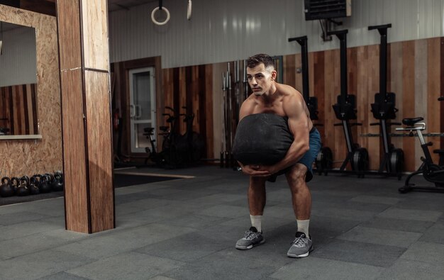 Atleta maschio muscolare che si esercita con la borsa pesante nella moderna palestra trasversale. Allenamento funzionale