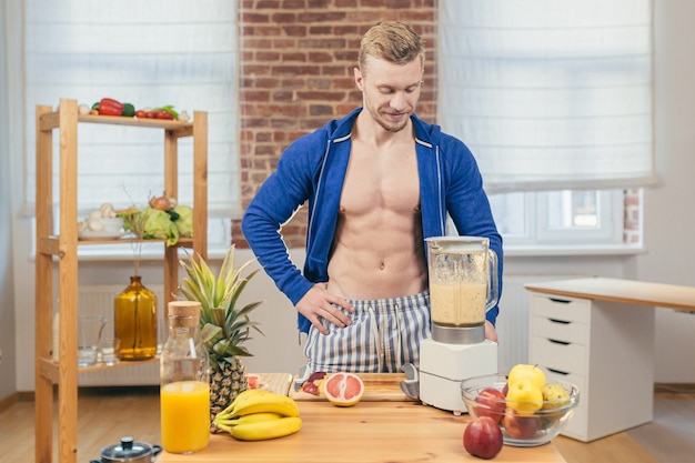 Atleta maschio prepara insalata e succhi di frutta fresca a casa in cucina