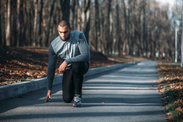 Atleta maschio si prepara a correre, allenamento all'aperto. Pareggiatore sull'allenamento mattutino. Uomo atletico che corre nel parco