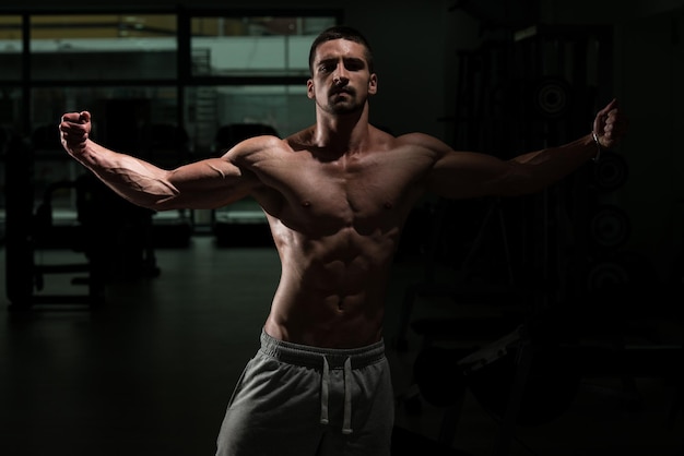 Atleta muscolare brutale bodybuilder emotivo in posa in una palestra buia
