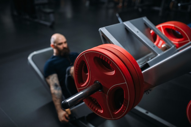 Atleta muscolare sulla macchina ginnica con bilanciere, allenamento in palestra.