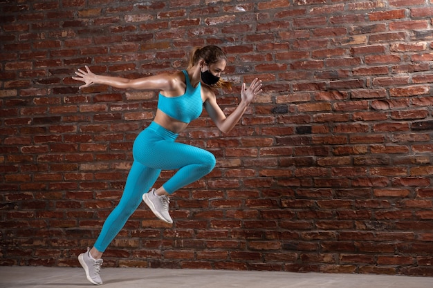 Atleta professionista femminile che si allena su un muro di mattoni che indossa una maschera facciale.