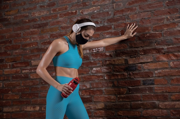 Atleta professionista femminile formazione su sfondo muro di mattoni indossando maschera facciale.