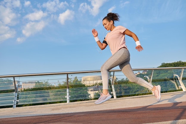 Atleta, sportiva, determinata donna attiva che pareggia su un tapis roulant sul ponte della città. Sport, fitness, allenamento cardio, stile di vita sano e concetto di perdita di peso