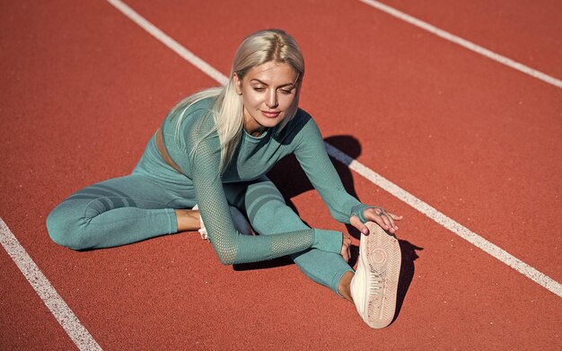 Atleta sportiva femminile in abbigliamento sportivo sullo stadio in fase di riscaldamento prima dell'allenamento fitness stretching