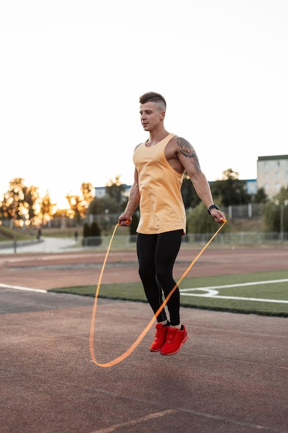 Atleta sportivo giovane bello in allenamento sportivo e salto con la corda allo stadio al tramonto