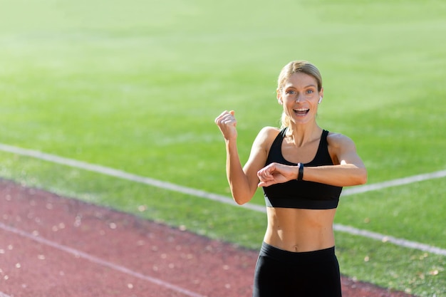 Atleta sportivo giovane donna in piedi nello stadio che indossa le cuffie e sorride alla macchina fotografica