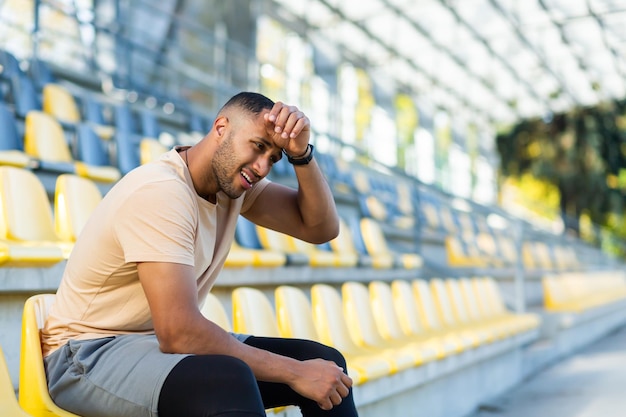 Atleta sportivo stanco e sconvolto seduto sullo stadio uomo afroamericano insoddisfatto del