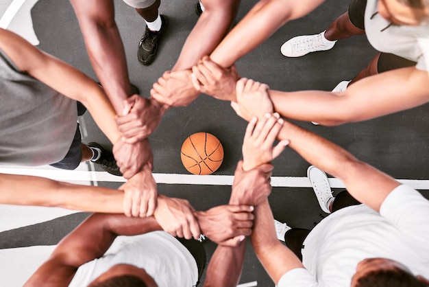 Atleti che mostrano fiducia e in piedi uniti Uomini che esprimono lo spirito di squadra con le mani giunte rannicchiate a una partita di basket Sportivi che tengono i polsi rannicchiati per supporto e unità durante la partita sportiva