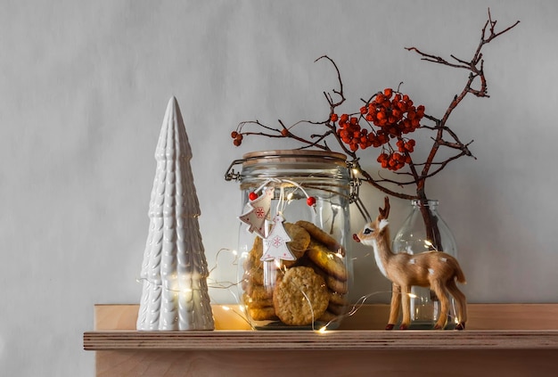 Atmosfera natalizia Una mensola di legno sulla parete con un albero di Natale in ceramica, un barattolo di biscotti e una ghirlanda luminosa