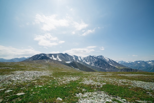 Atmosferico paesaggio alpino con prato sassoso con erba verde e grandi creste di montagna. Meravigliose montagne innevate sotto il cielo blu. Luogo idilliaco negli altopiani. Maestoso scenario in alta quota.