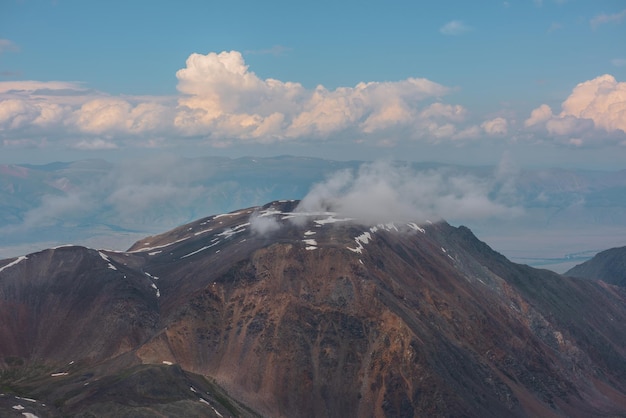 Atmosferico paesaggio montano con nuvole basse sulla cima di un'alta montagna con neve sotto il cielo nuvoloso Drammatica vista aerea su un grande picco di montagna rocciosa con nuvole basse Bella vista dall'alto verso il pinnacolo