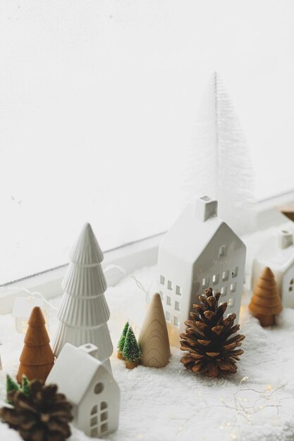 Atmosferico villaggio invernale in miniatura Eleganti graziose casette in ceramica e alberi di Natale in legno su una soffice coltre di neve con luci incandescenti Natale moderno sfondo bianco Buone vacanze