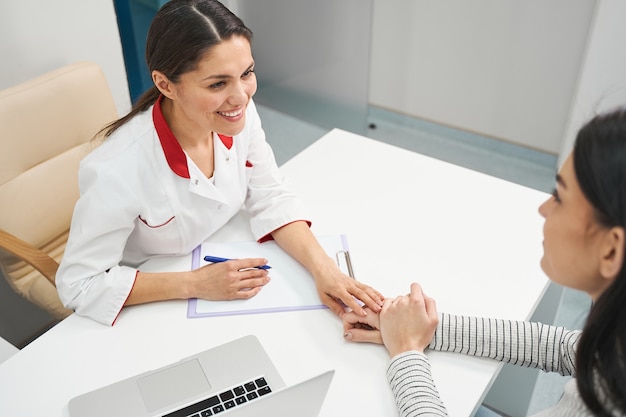 Attenta ragazza bruna che è in tutte le orecchie mentre ascolta la prescrizione professionale, visitando il suo medico