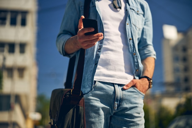 Attento giovane in piedi per strada e guardando il suo gadget mentre controlla la posta elettronica