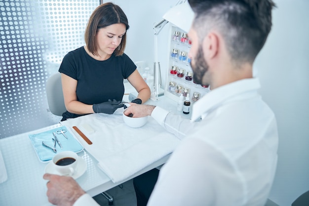 Attento maestro di manicure seduto sul posto di lavoro mentre esegue una procedura professionale