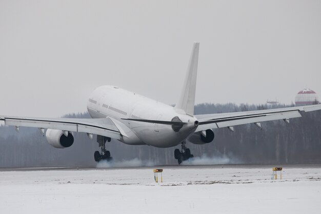 Atterraggio di aeroplano sulla pista con fumo dal telaio nel periodo invernale