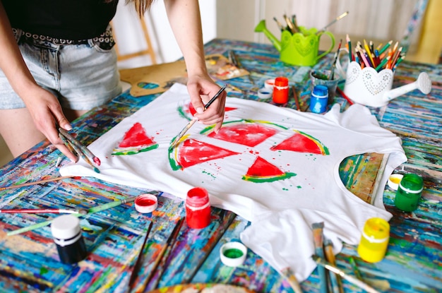 Attingere vestiti. La ragazza disegna su una maglietta bianca.