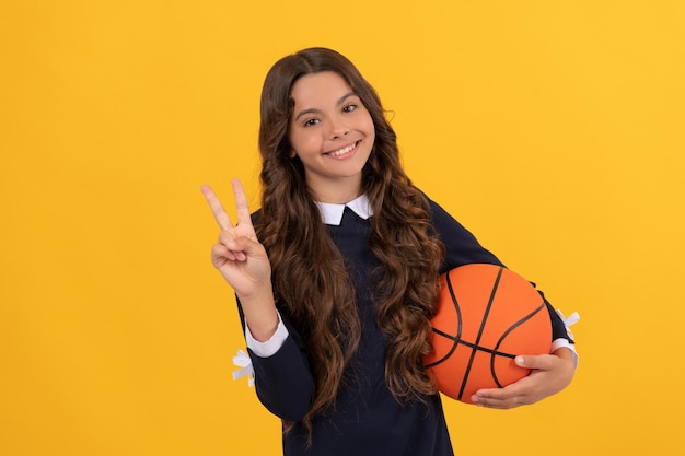 Attività estiva. ragazza adolescente allegra con palla da basket. bambino giocatore di basket. scuola sportiva. bambino sulla lezione di allenamento fisico. di nuovo a scuola. gesto di pace. sport e hobby.