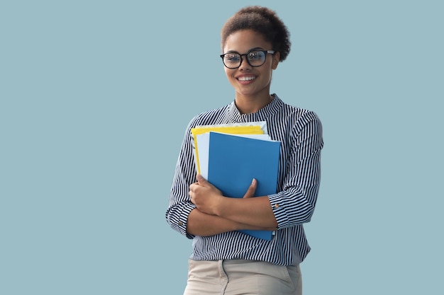 Attractiva donna d'affari afroamericana che guarda la telecamera e sorride mentre si trova sullo sfondo blu