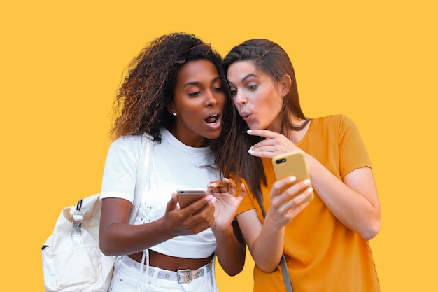 Attractive giovani donne felici amiche che parlano con i telefoni cellulari sullo sfondo giallo