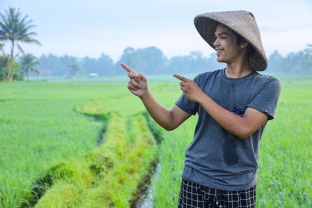 Attraente allegro giovane agricoltore asiatico in piedi sorridente di lato e puntando il dito verso il lato