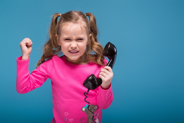 Attraente bambina carina in camicia rosa con scimmia e pantaloni blu parla un telefono