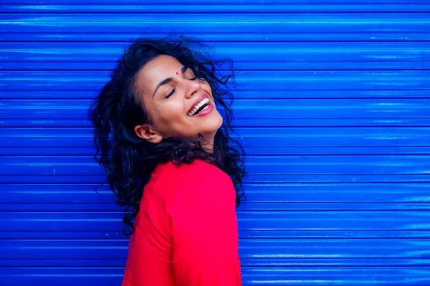 Attraente bella giovane donna ispanica latina felice con bindi in teak sulla fronte sorridente su sfondo blu wall street