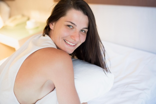 Attraente bella giovane donna sorridente sveglia al mattino sul letto bianco