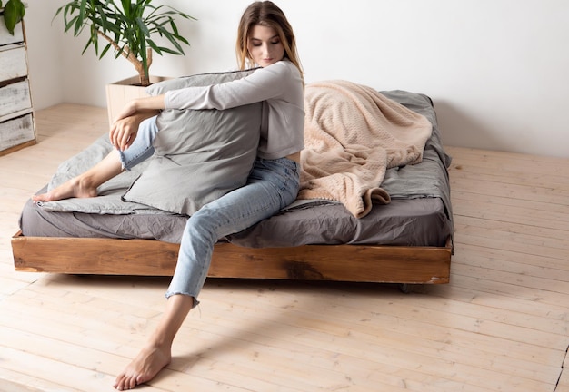 Attraente bionda felice sexy con un bel sorriso in azzurro e jeans seduto sul letto