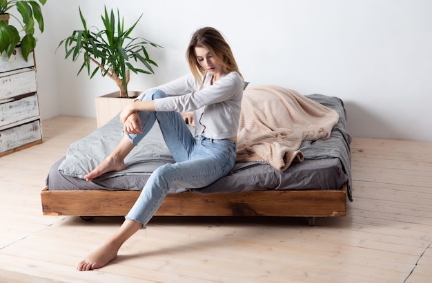 Attraente bionda felice sexy con un bel sorriso in azzurro e jeans sul letto