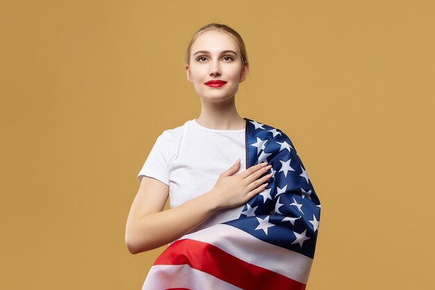 Attraente bionda posa con orgoglio con una bandiera americana. servizio fotografico in studio su sfondo giallo.