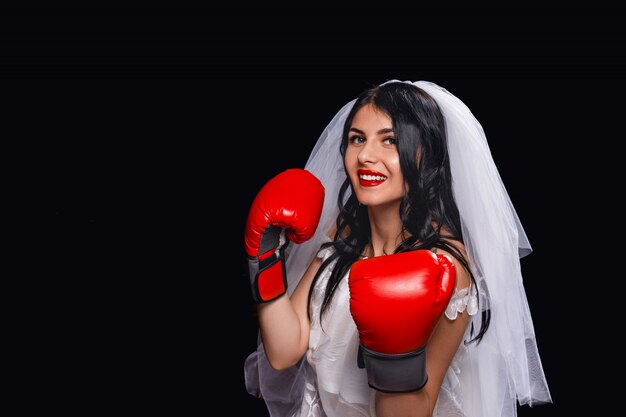 Attraente bruna con rossetto rosso, in abito da sposa, velo e guantoni da boxe.