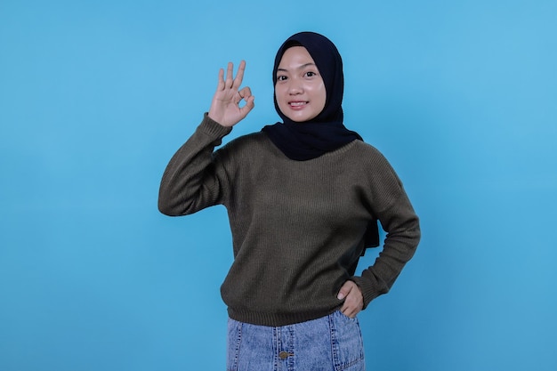 Attraente bruna felice con l'uso dell'hijab, che mostra un gesto ok sulla parete blu