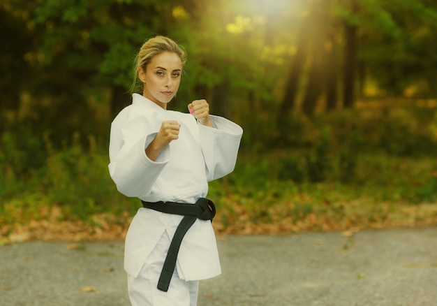 Attraente combattente femminile in un kimono bianco con una cintura nera si trova in una posizione di combattimento all'aperto