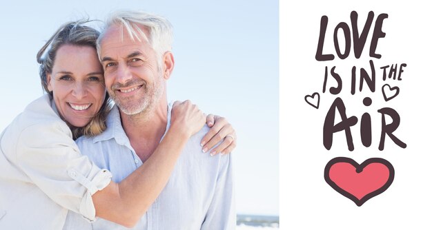 Attraente coppia che abbraccia in spiaggia sorridere alla telecamera contro l'amore è nell'aria