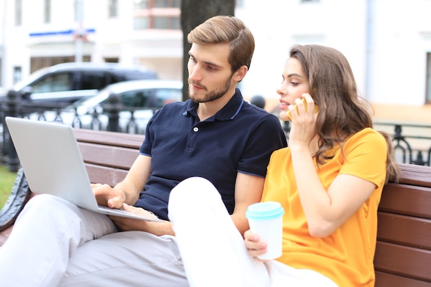 Attraente coppia giovane utilizzando il computer portatile mentre è seduto su una panchina all'aperto.