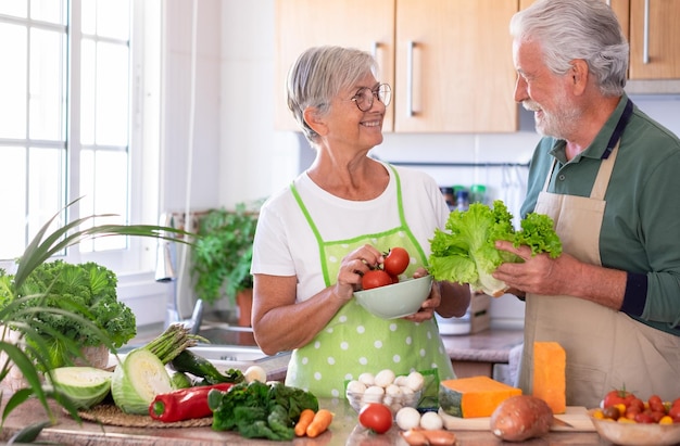 Attraente coppia senior che lavora insieme nella cucina di casa preparando verdure Coppia anziana sorridente che gode di uno stile di vita sano guardando negli occhi