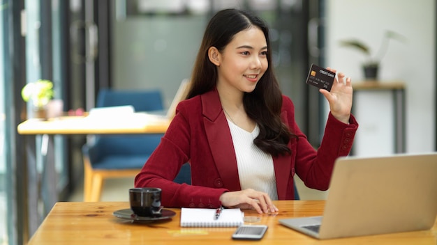 Attraente dipendente di sesso femminile in possesso di carta di credito e si siede davanti alla scrivania del suo computer portatile in ufficio. internet banking, concetto di pagamento online.