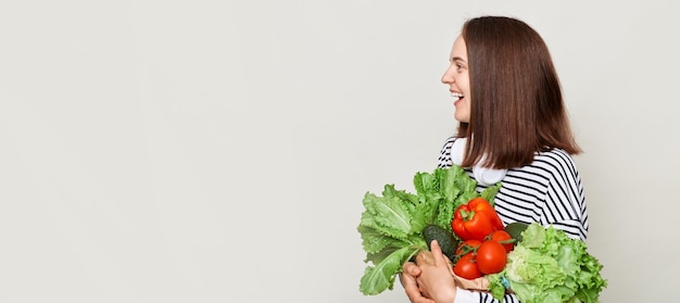 Attraente donna abbraccia la posa di verdure fresche isolato su sfondo bianco distogliendo lo sguardo formica pubblicità area copia spazio per il testo promozionale
