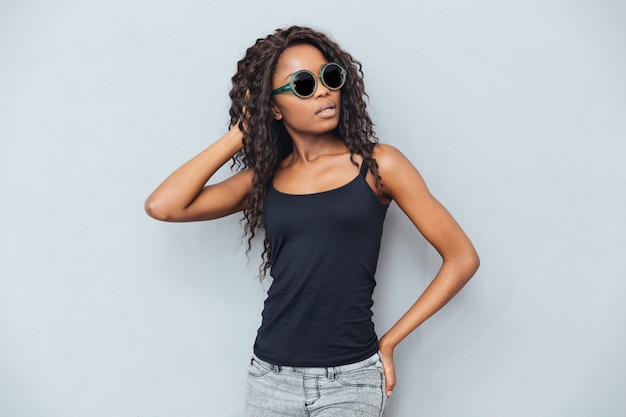 Attraente donna afro con gli occhiali in posa sul muro grigio gray