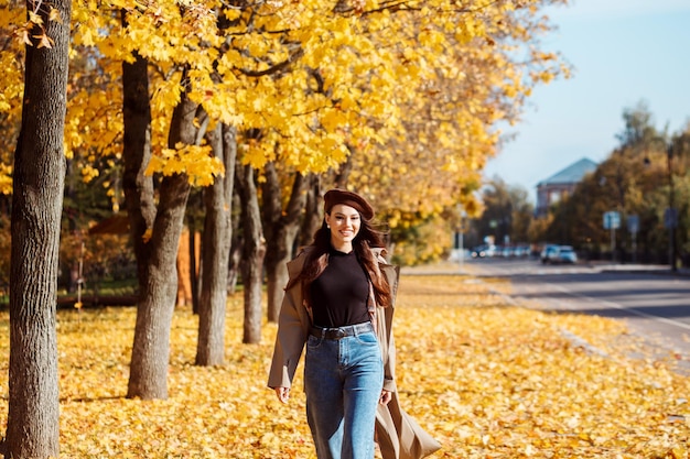 Attraente donna allegra in berretto marrone che trascorre del tempo all'aperto in autunno nel parco