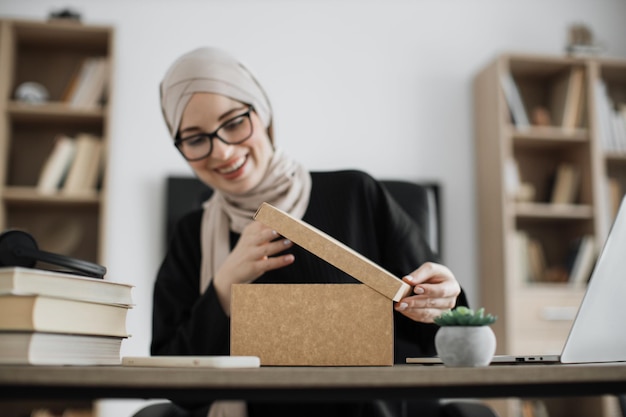 Attraente donna araba con espressione facciale sorpresa che guarda dentro la scatola di carta