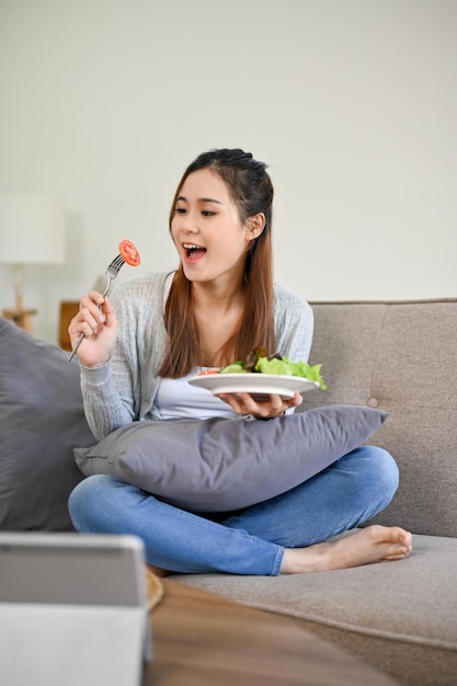 Attraente donna asiatica si diverte a mangiare la sua insalata sana e biologica nel suo soggiorno