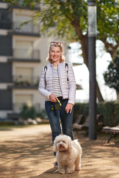 Attraente donna bionda di mezza età che cammina con il cane in città d'estate.