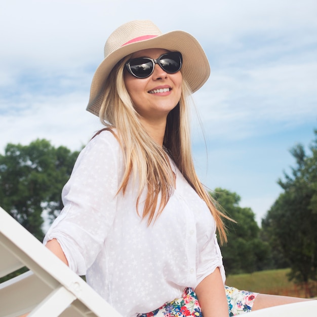 Attraente donna bionda sorridente in cappello da sole e occhiali da sole