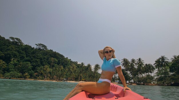 Attraente donna bionda sportiva con occhiali da sole righe rosa canoa di plastica lungo l'acqua di mare