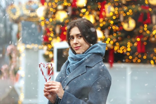 Attraente donna bruna con caramelle a forma di cuore durante la nevicata