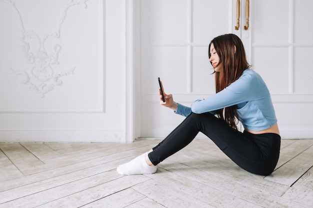 Attraente donna caucasica utilizzando il telefono cellulare dopo l'allenamento fitness a casa.