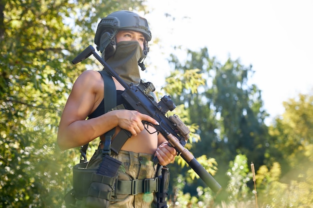 Attraente donna coraggiosa militare con una pistola nella foresta, sopravvivenza nella foresta selvaggia